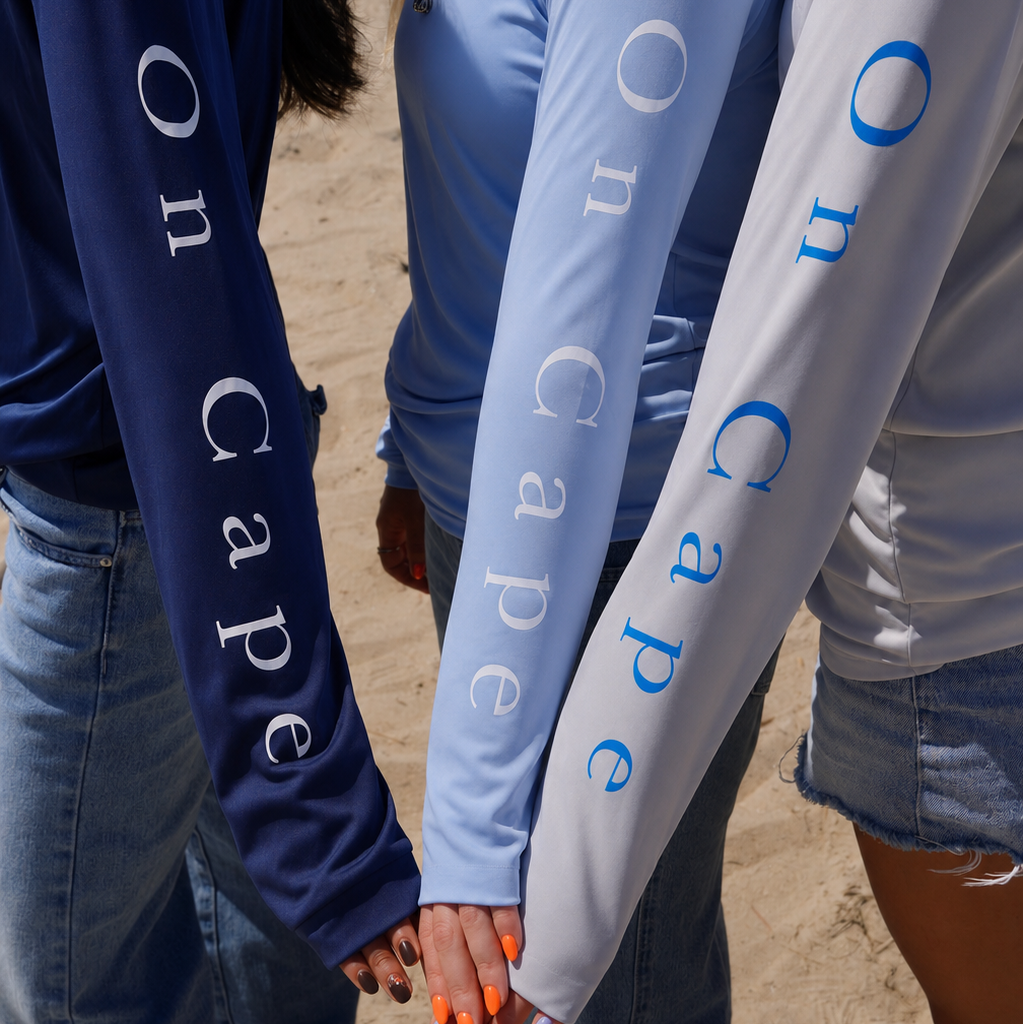 Three people wearing long-sleeve shirts with 'On Cape' text on a sandy background